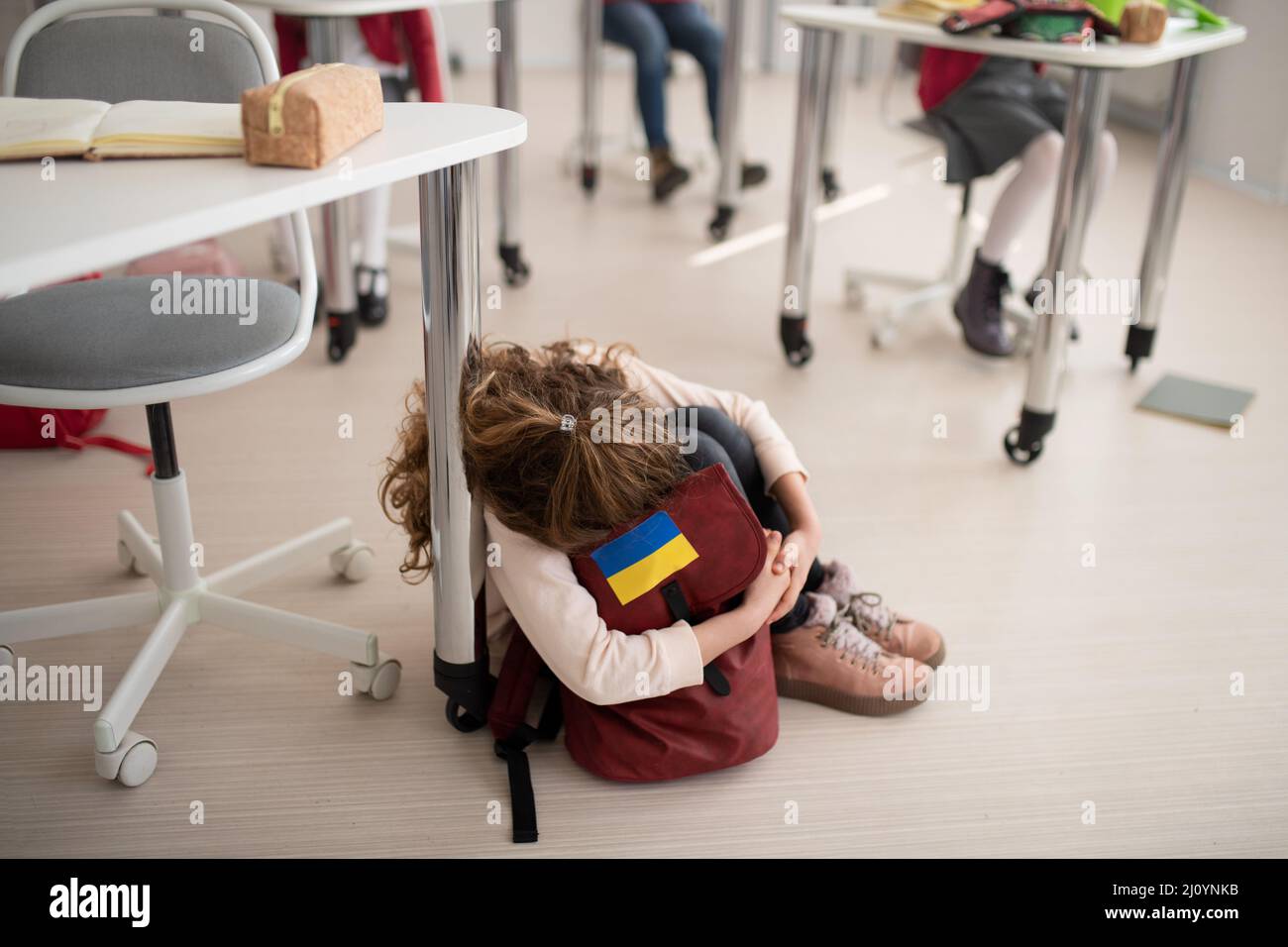 Piccola ragazza Ucraina triste seduta sul pavimento a scuola, concetto di iscrizione dei capretti ucraini alle scuole. Foto Stock