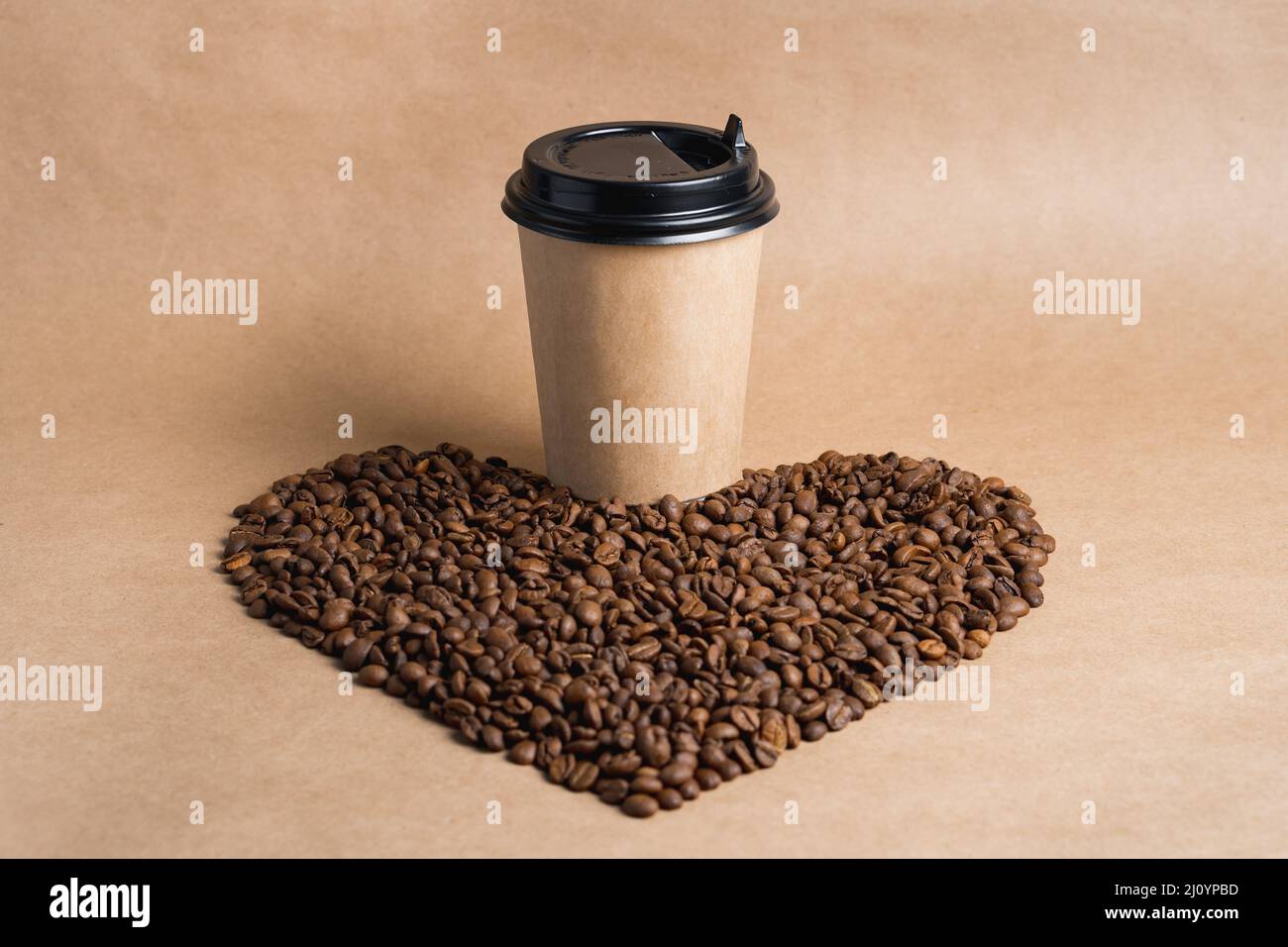 La tazza da caffè in carta marrone da asporto con tappo nero si trova sui chicchi tostati a forma di cuore. Mock up Foto Stock