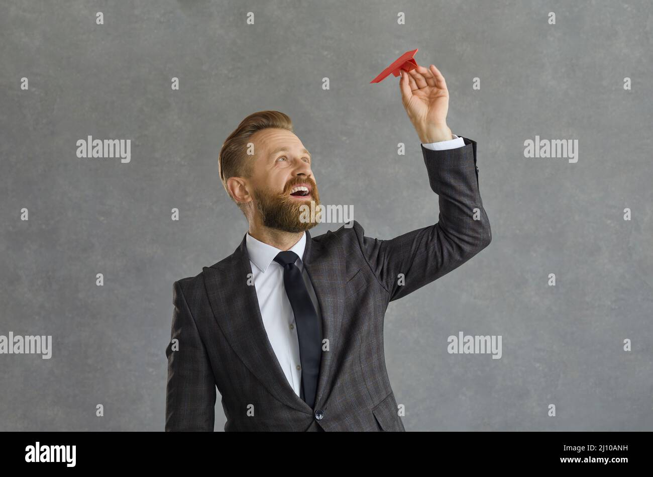 Ritratto di un uomo d'affari caucasico di successo che sta per correre un aereo di carta su uno sfondo grigio. Foto Stock