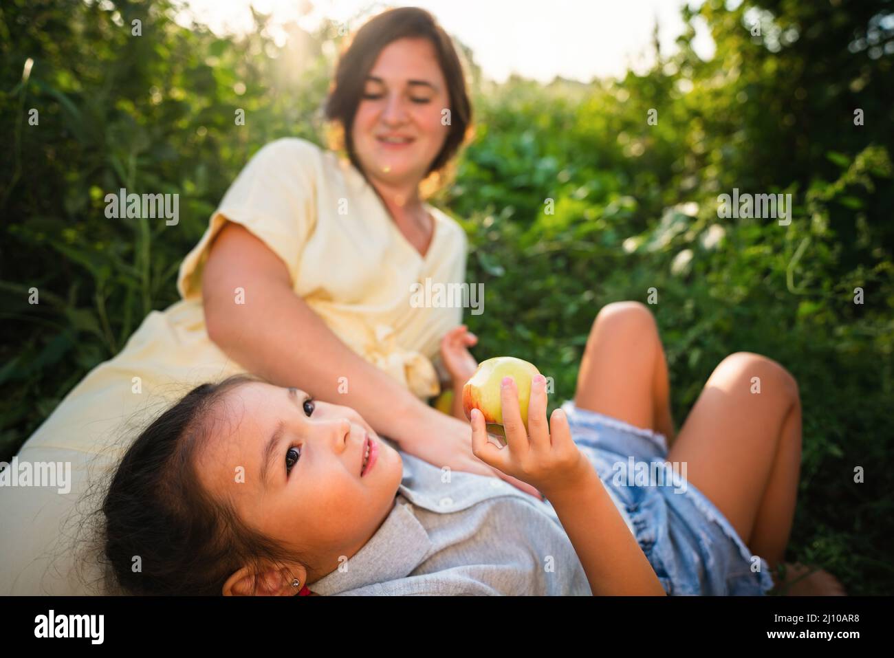 Madre europea e sua figlia asiatica nel giardino delle mele in estate Foto Stock