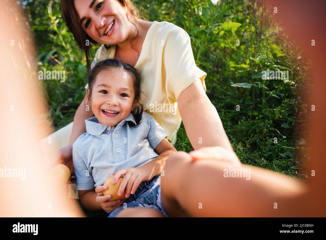Madre europea e sua figlia asiatica nel giardino delle mele in estate Foto Stock