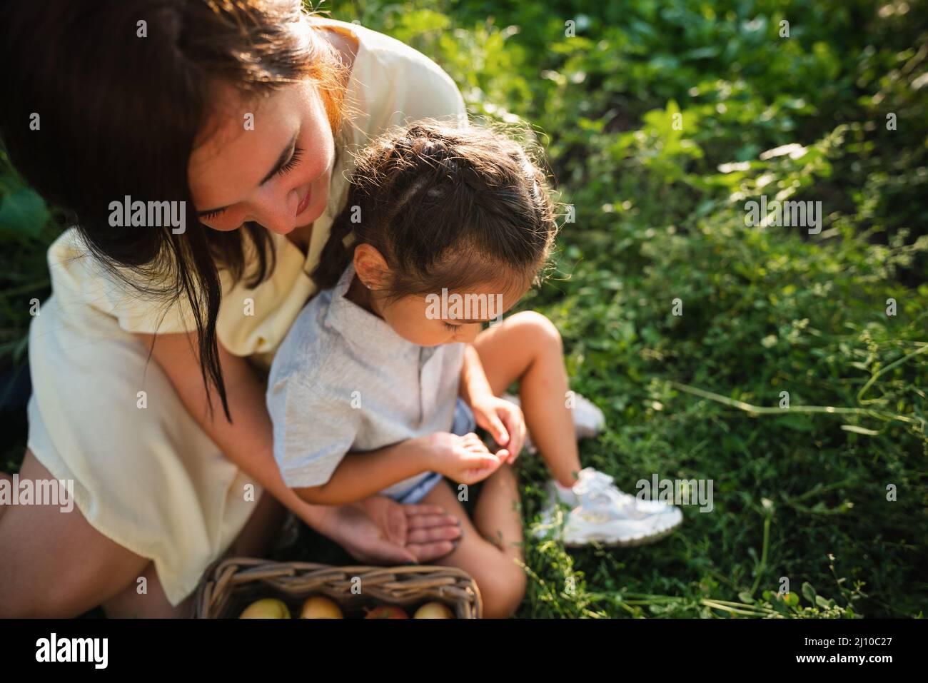 Madre europea e sua figlia asiatica nel giardino delle mele in estate Foto Stock
