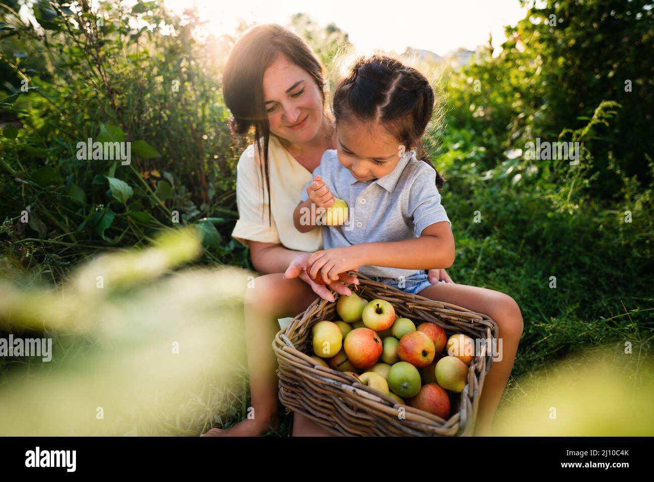 Madre europea e sua figlia asiatica nel giardino delle mele in estate Foto Stock
