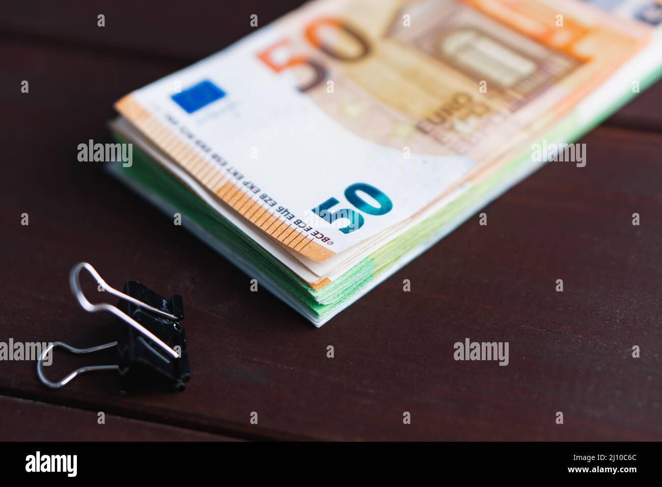 Pila di banconote in euro di carta e graffette su tavola di legno. Mucchio di soldi. Messa a fuoco selettiva Foto Stock