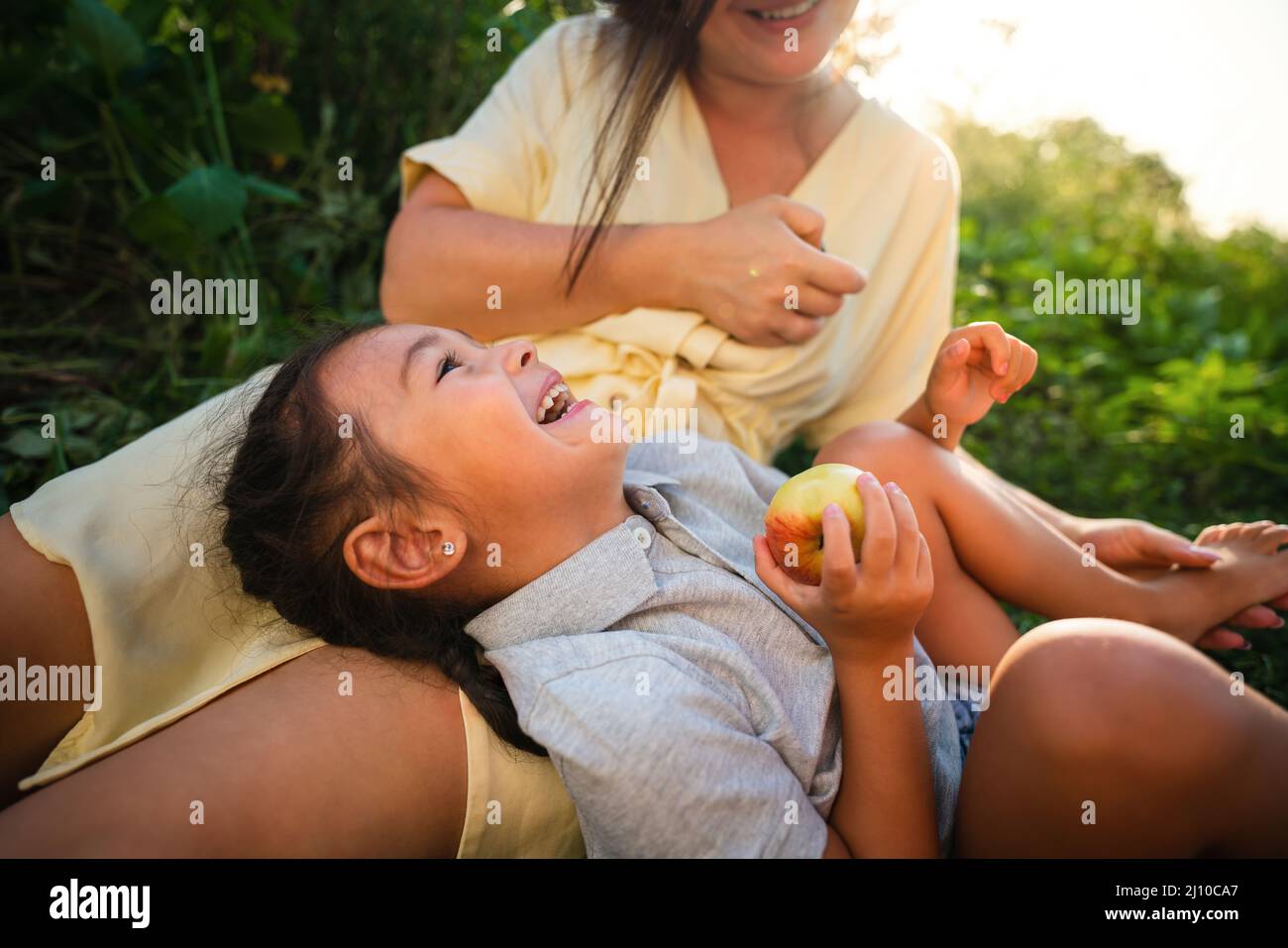 Madre europea e sua figlia asiatica nel giardino delle mele in estate Foto Stock