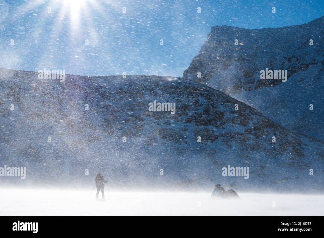 Una scialpinista solista in spindrift evidenziata dai raggi del sole sulle montagne norvegesi Foto Stock