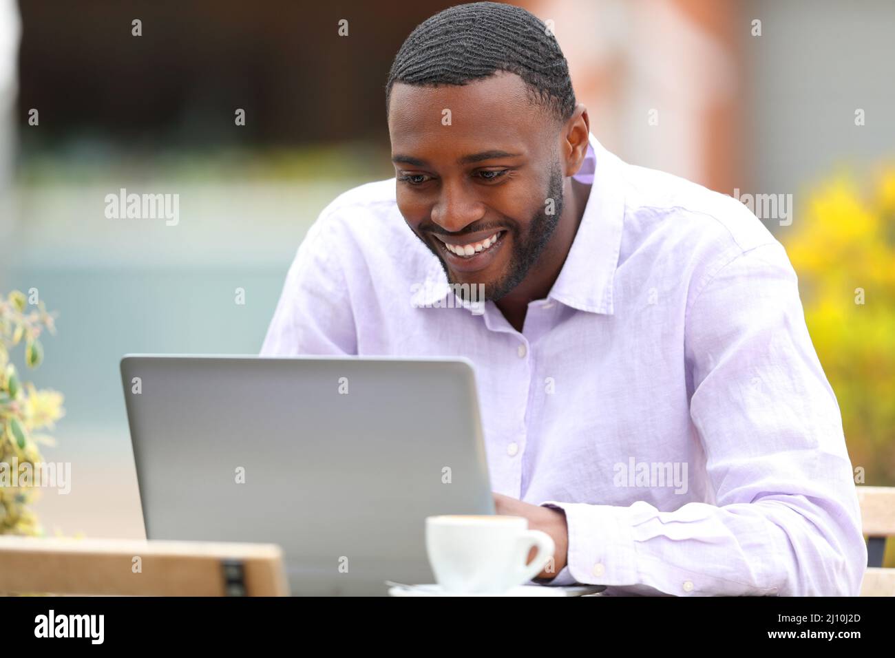 Uomo felice con la pelle nera che controlla il contenuto del laptop in un bar terrazza Foto Stock
