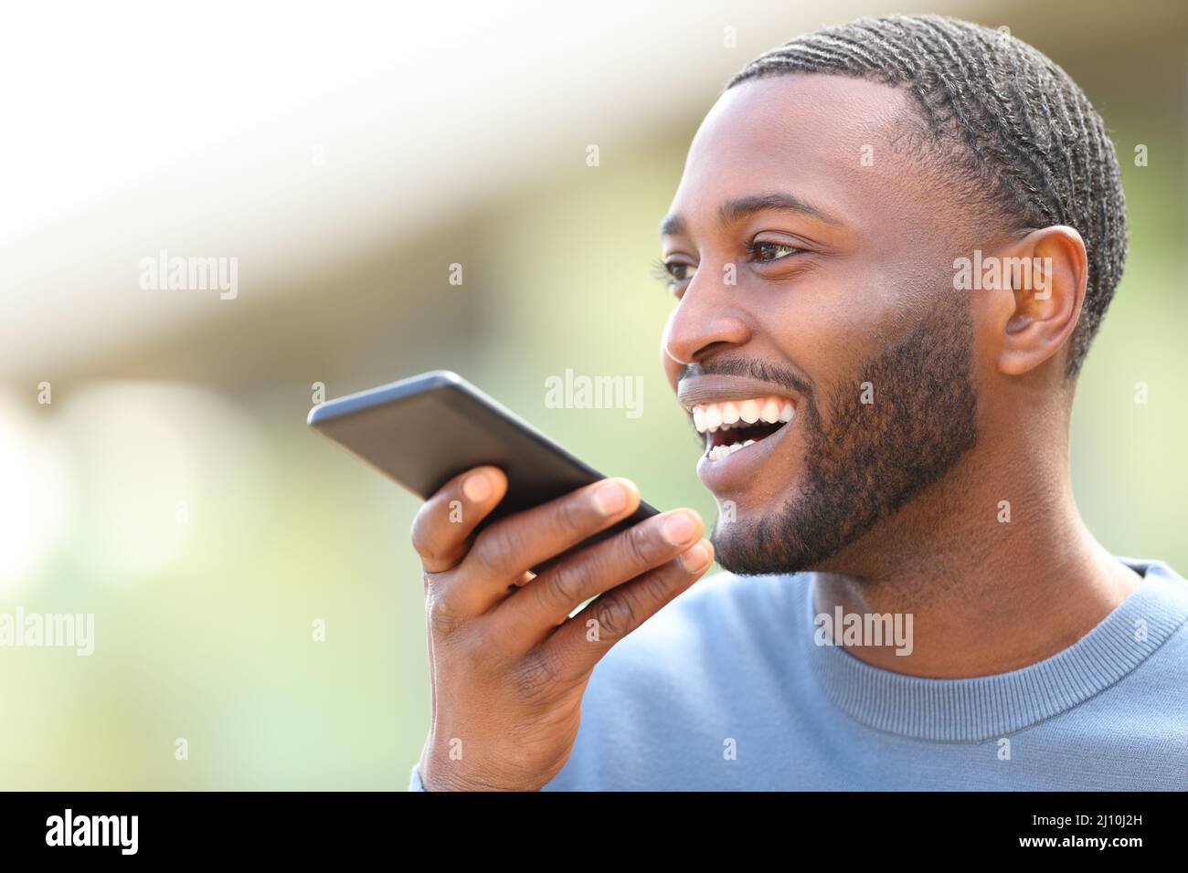 Uomo felice con la pelle nera dettare il testo sul telefono cellulare in strada Foto Stock