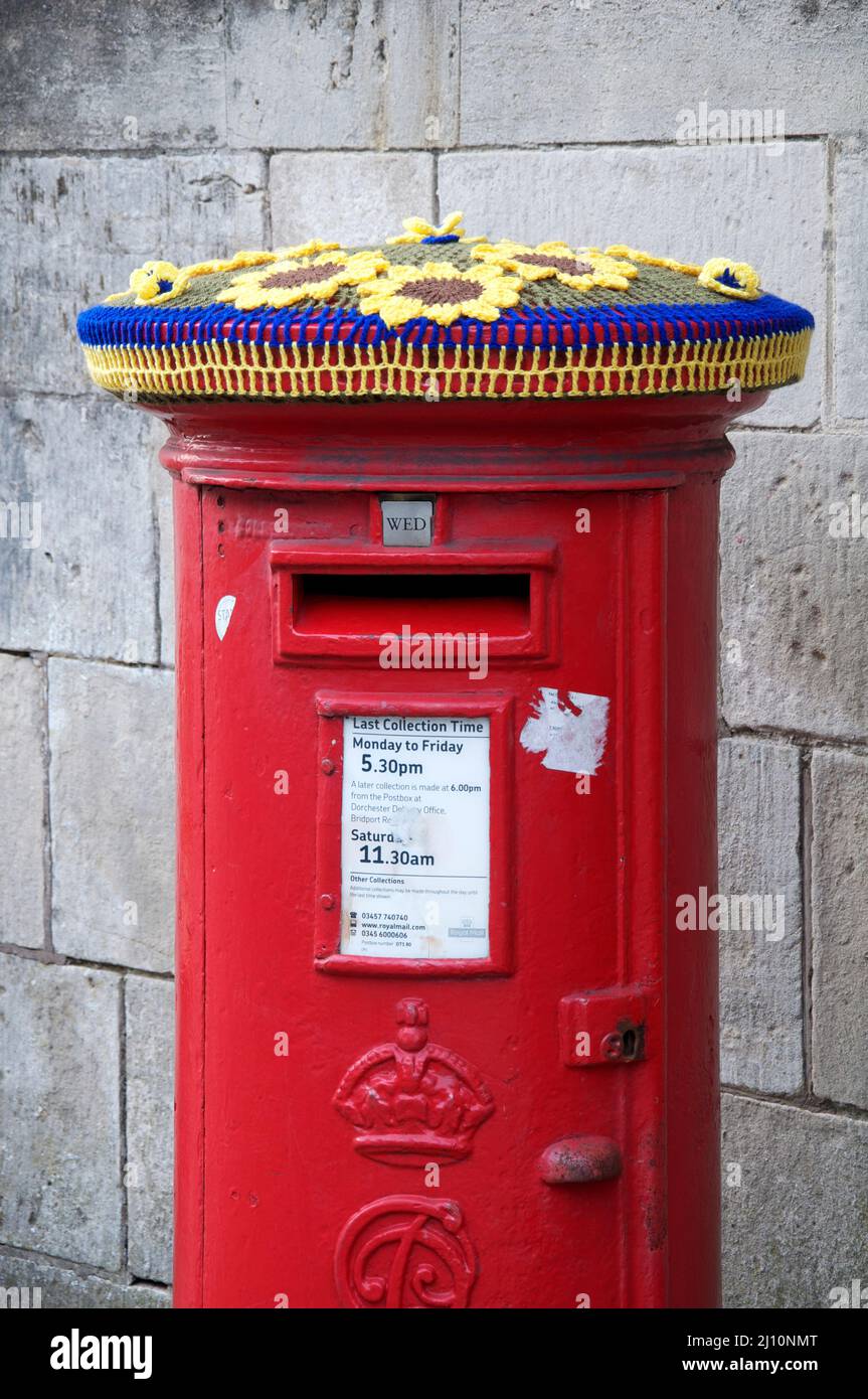 Colori ucraini blu e giallo: Cappello di lana lavorato a maglia decorare un pillarbox rosso. In solidarietà con il popolo ucraino. Dorchester, Dorset, Regno Unito. Foto Stock