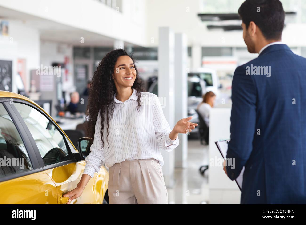 Signora mediorientale che sceglie la nuova automobile, avendo colloquio con il responsabile di vendite Foto Stock