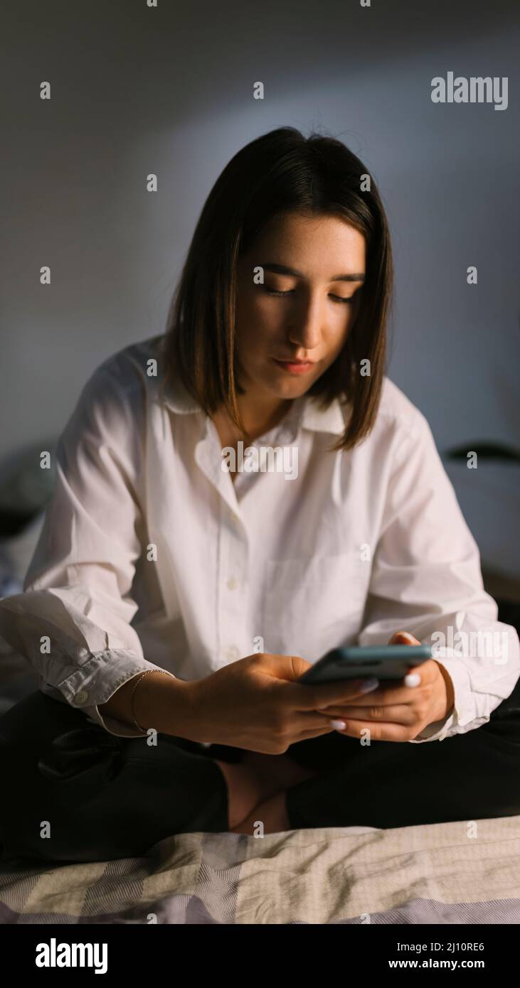 Donna seduta sul letto guardando il telefono Foto Stock