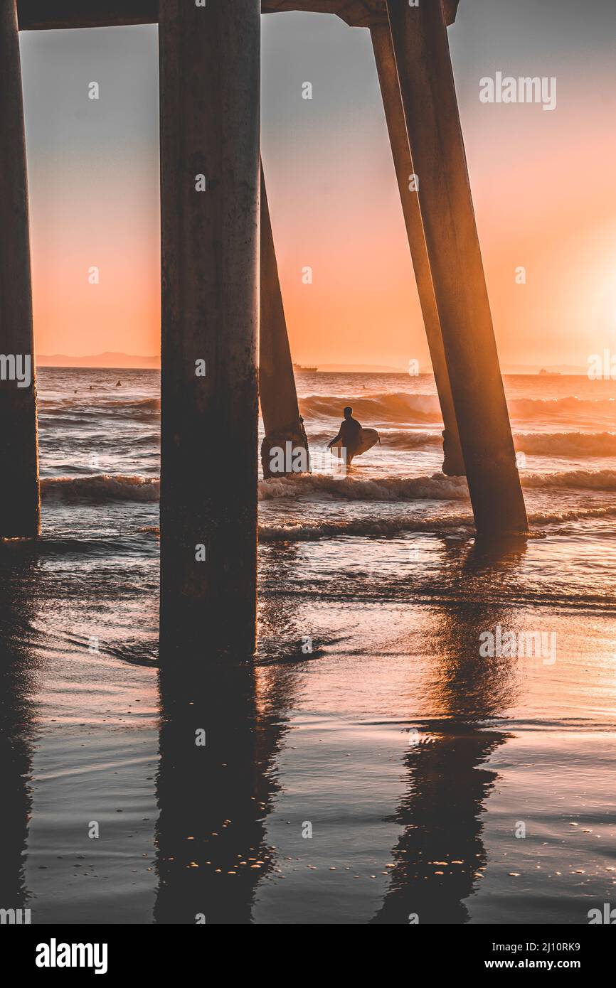 Un surfista che cattura le onde del tramonto sotto un molo Foto Stock