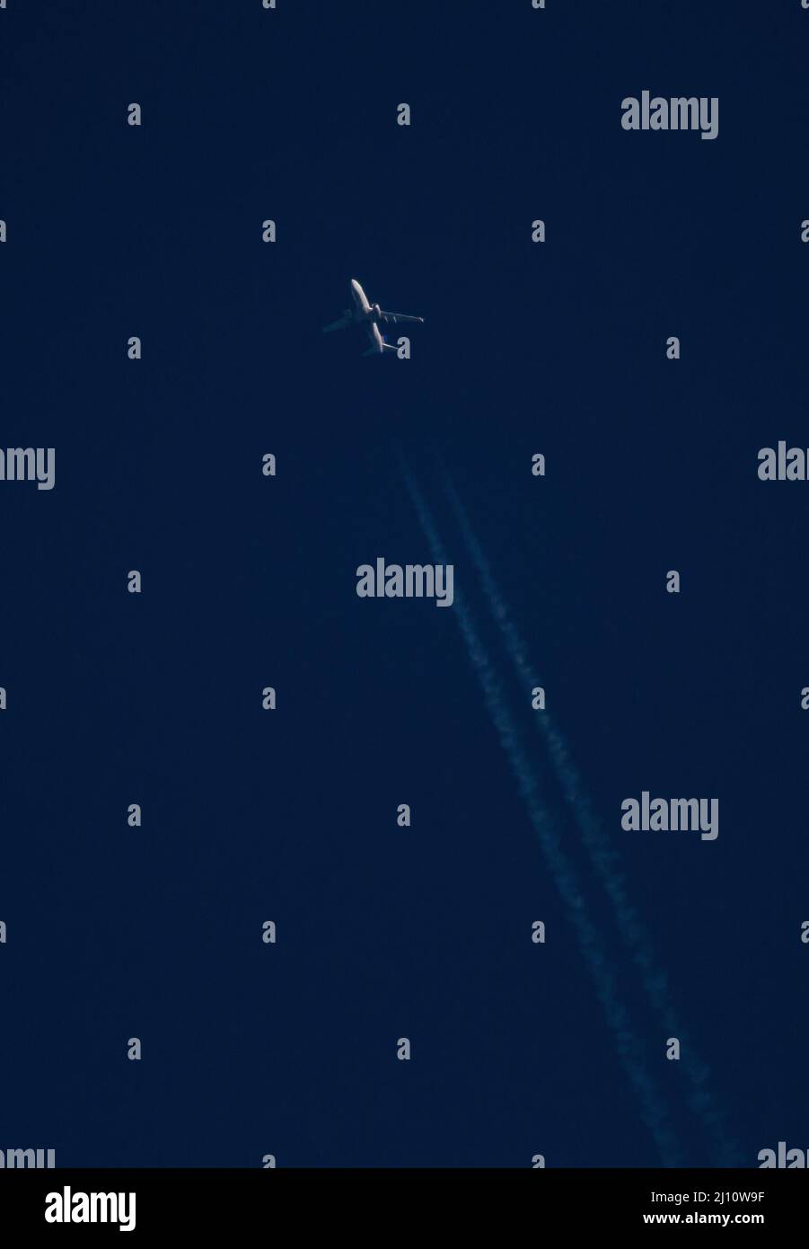 Un aereo di linea commerciale ad alta quota con contrali passa attraverso un cielo blu profondo al tramonto. Foto Stock