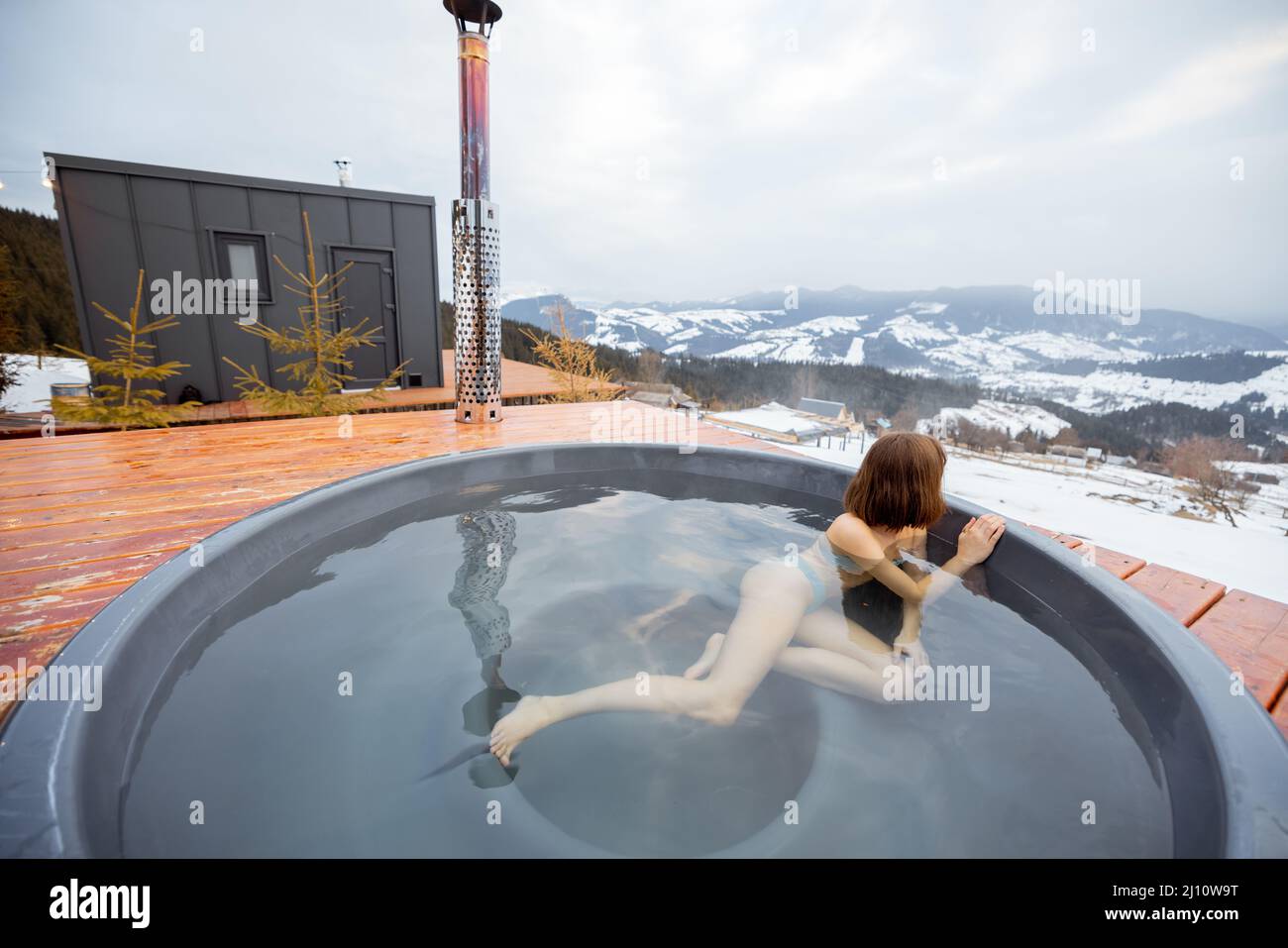 La donna nuota nel bagno caldo mentre riposa in una piccola casa moderna in montagna Foto Stock