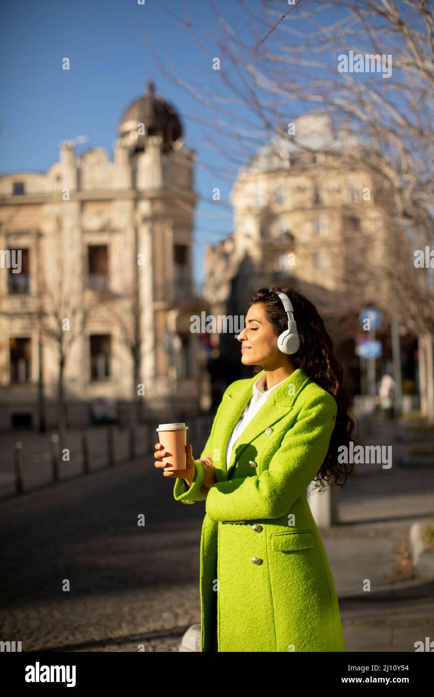 Bella giovane donna che ascolta musica con le cuffie per strada Foto Stock