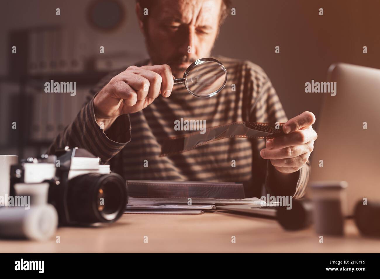 Fotografo che rivede vecchia telecamera analogica 35 pellicola negativa sul suo posto di lavoro, fuoco selettivo Foto Stock