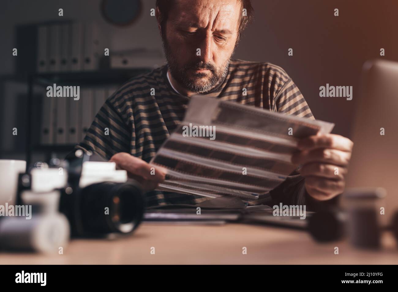 Fotografo che rivede vecchia telecamera analogica 35 pellicola negativa sul suo posto di lavoro, fuoco selettivo Foto Stock