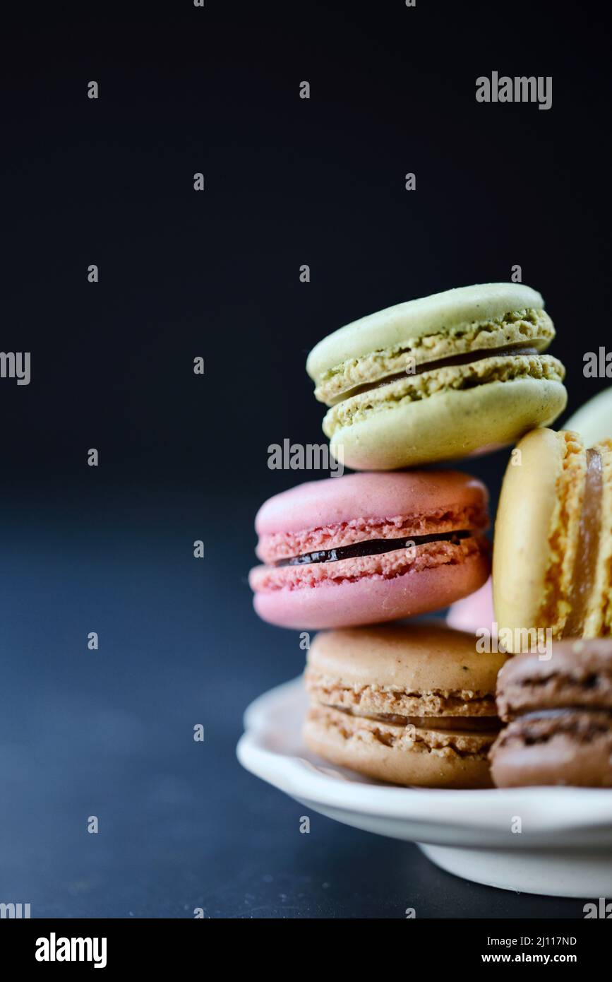 Mucchio di biscotti al lampone, pistacchio, cioccolato e limone macaron su un piatto con fondo nero. Foto Stock Mucchio di biscotti al lampone, pistacchio, cioccolato e limone macaron su un piatto con fondo nero. Foto Stock