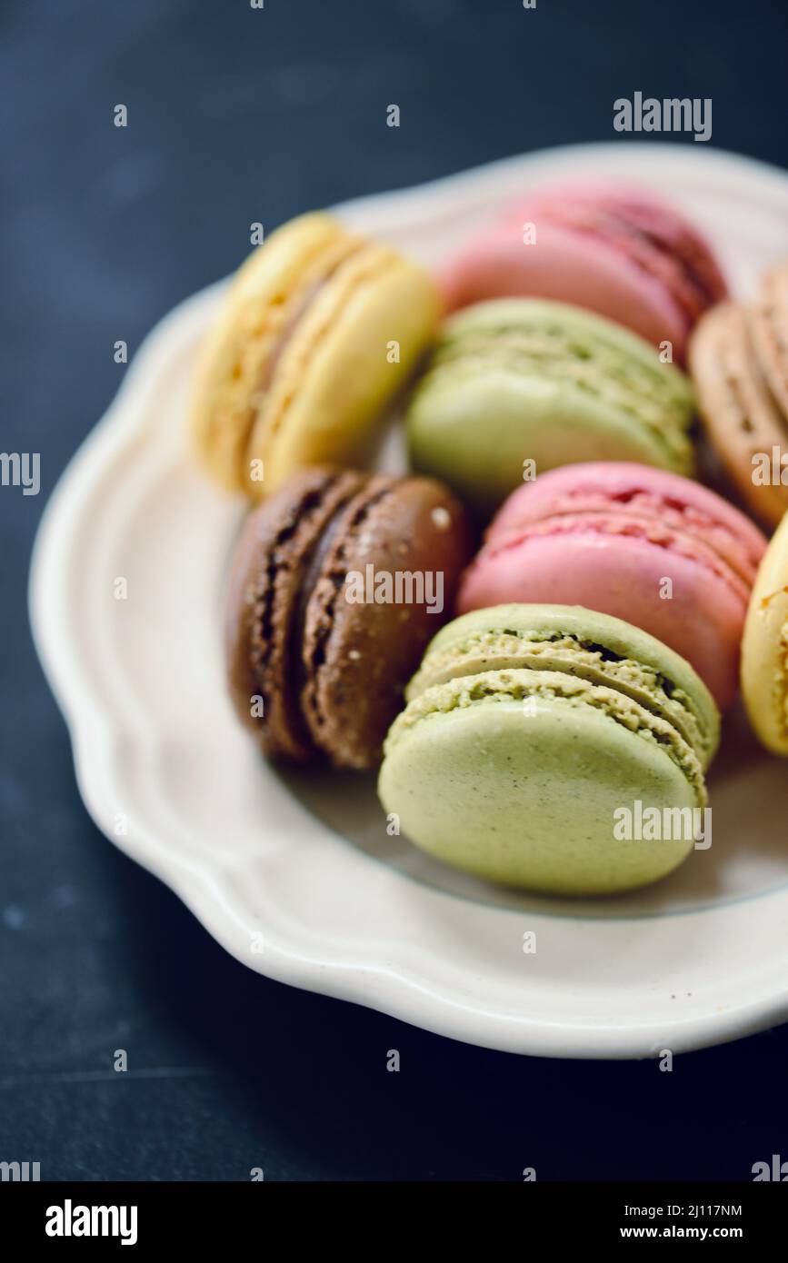 Lampone, pistacchio, cioccolato e macaron francese al limone su un piatto bianco d'annata con sfondo nero Foto Stock Lampone, pistacchio, cioccolato e macaron francese al limone su un piatto bianco d'annata con sfondo nero Foto Stock