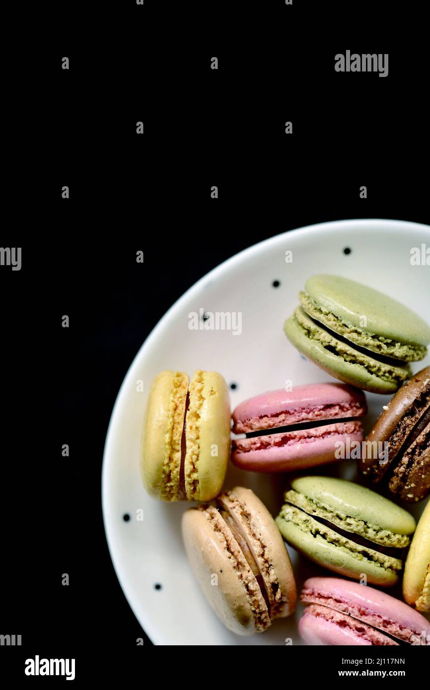 Un piatto di lamponi, caramello, limone e pistacchio macaron su sfondo nero Foto Stock Un piatto di lamponi, caramello, limone e pistacchio macaron su sfondo nero Foto Stock