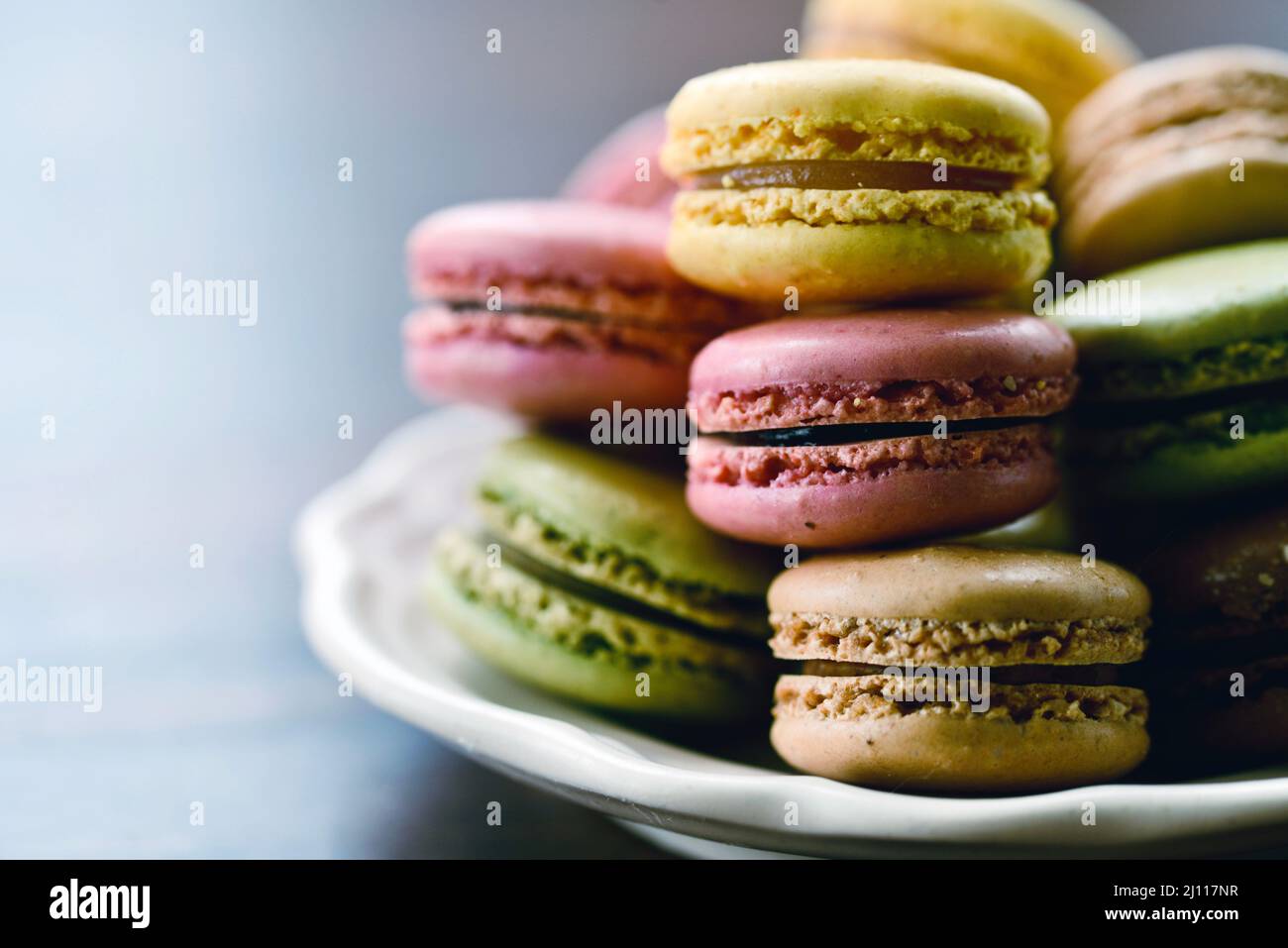 Un mucchio di biscotti francesi di macaron accatastati su un piatto su un tavolo di legno in luce naturale Foto Stock Un mucchio di biscotti francesi di macaron accatastati su un piatto su un tavolo di legno in luce naturale Foto Stock