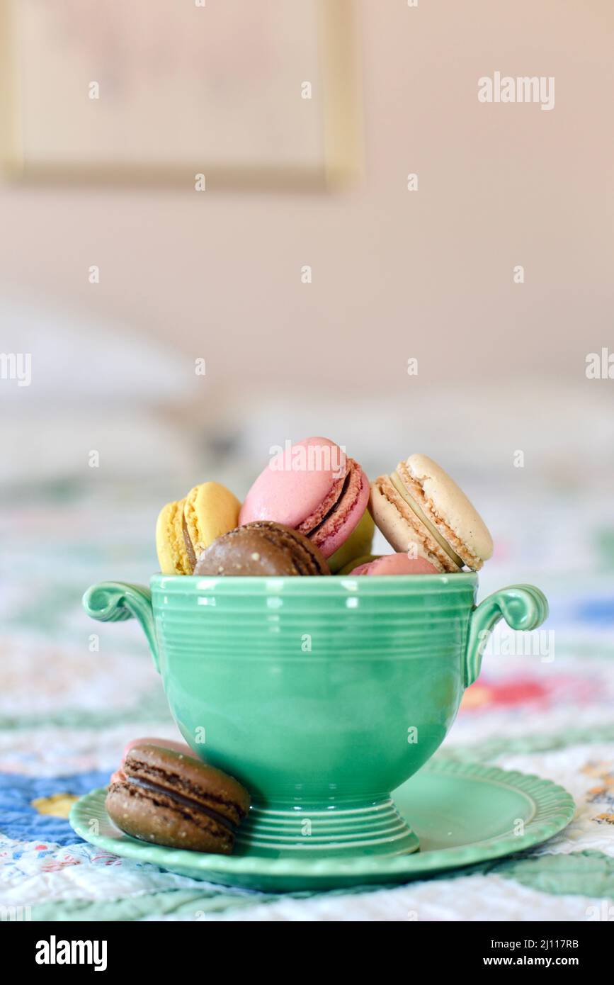 Primo piano di biscotti francesi di macaron in una ciotola verde d'annata su un letto. Foto Stock Primo piano di biscotti francesi di macaron in una ciotola verde d'annata su un letto. Foto Stock