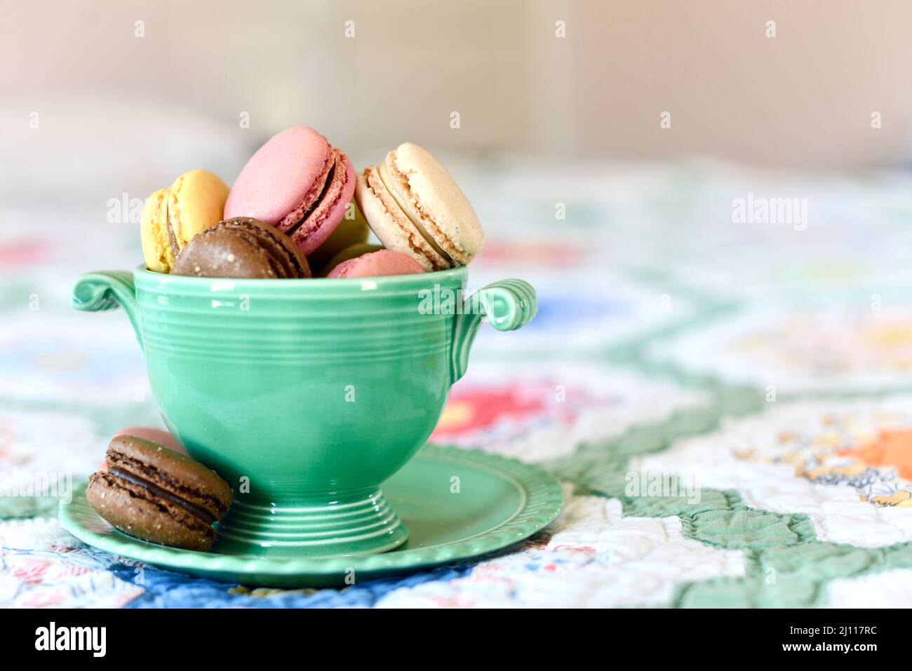 Primo piano di biscotti francesi di macaron in una ciotola verde d'annata su un letto. Foto Stock Primo piano di biscotti francesi di macaron in una ciotola verde d'annata su un letto. Foto Stock