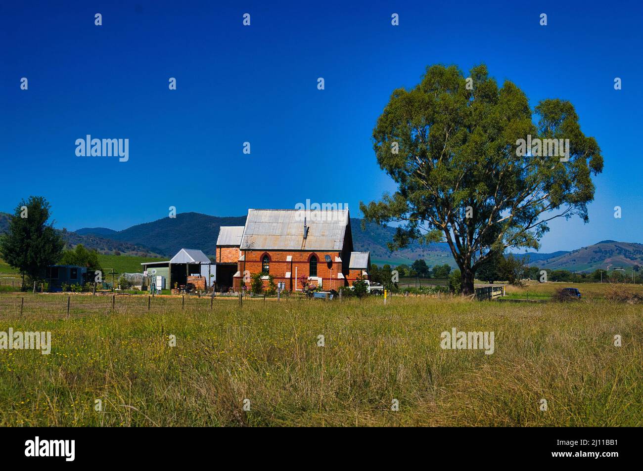 Ex chiesa, trasformata in una casa annesso fattoria, in piedi accanto ad un albero alto. Kiewa Valley vicino a Tawonga, Victoria, Australia Foto Stock