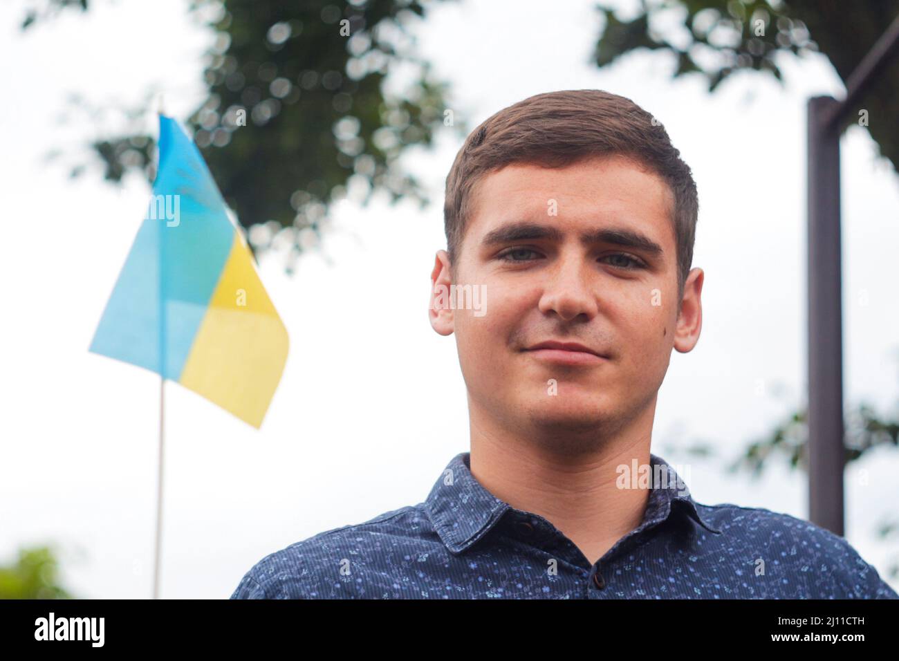 Uomo ucraino. Giovane uomo sorriso con bandiera ucraina. Nessuna guerra. Sostegno all'Ucraina. Spirito patriottico crescente mano di bandiera Ucraina. Libertà ucraina Foto Stock