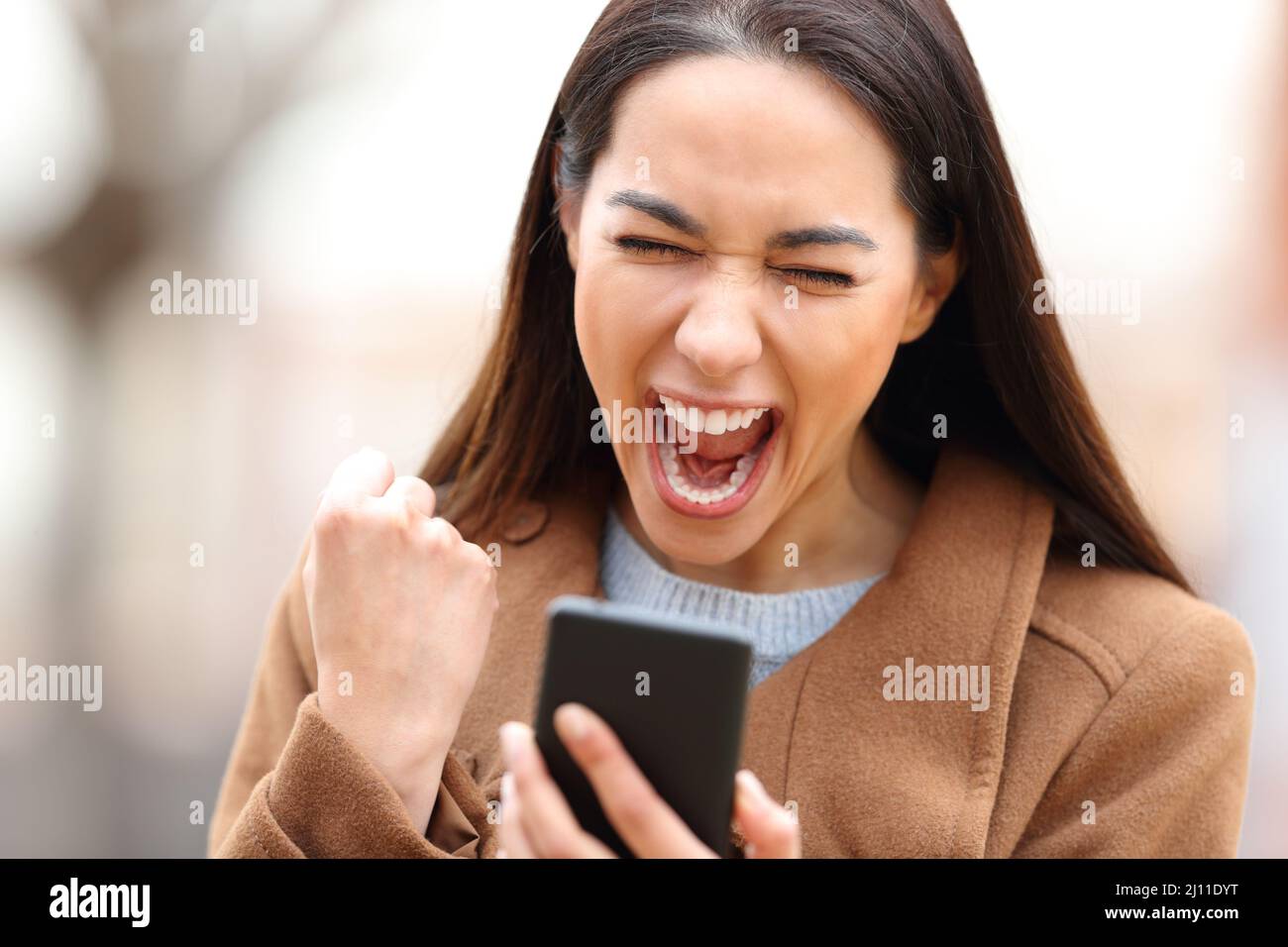 Donna eccitata in inverno controllare il telefono cellulare in un parco Foto Stock