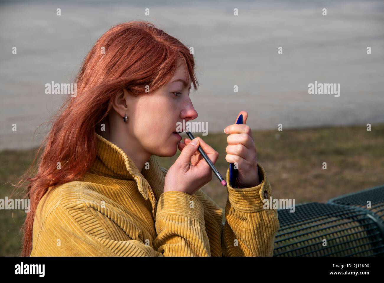 Vista laterale di una donna dai capelli rossi che si forma, colorando le labbra Foto Stock