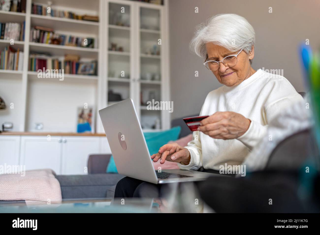 Donna anziana che fa shopping online su laptop a casa Foto Stock