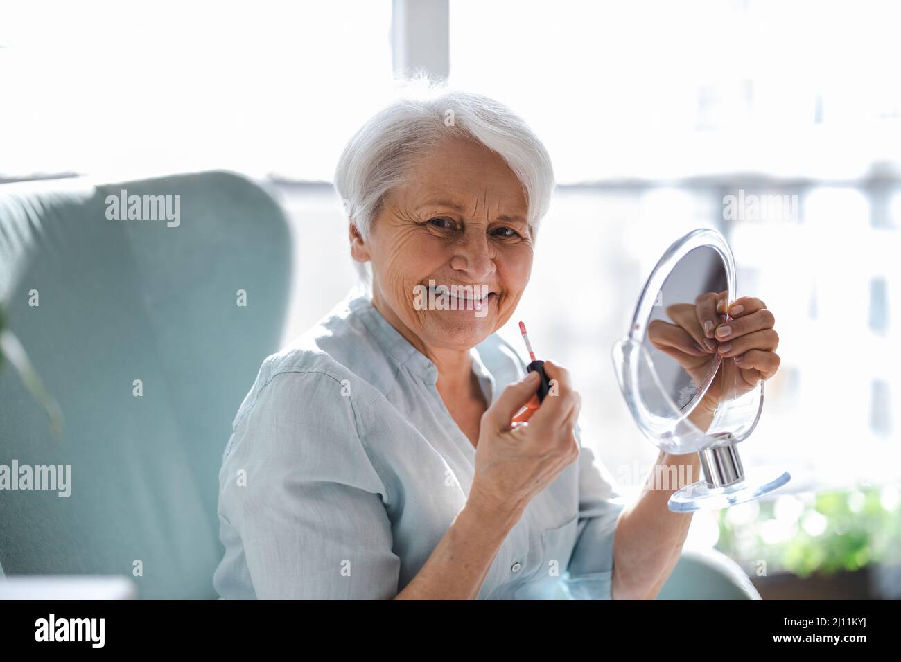Donna anziana che fa il trucco di fronte allo specchio Foto Stock
