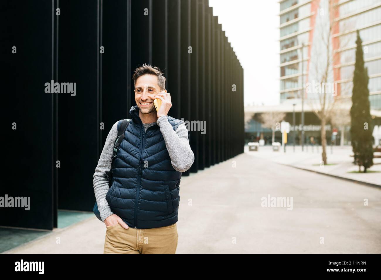 Uomo libero in abiti casual, utilizzando smartphone, edificio moderno sullo sfondo. Lavorare in remoto in città Foto Stock