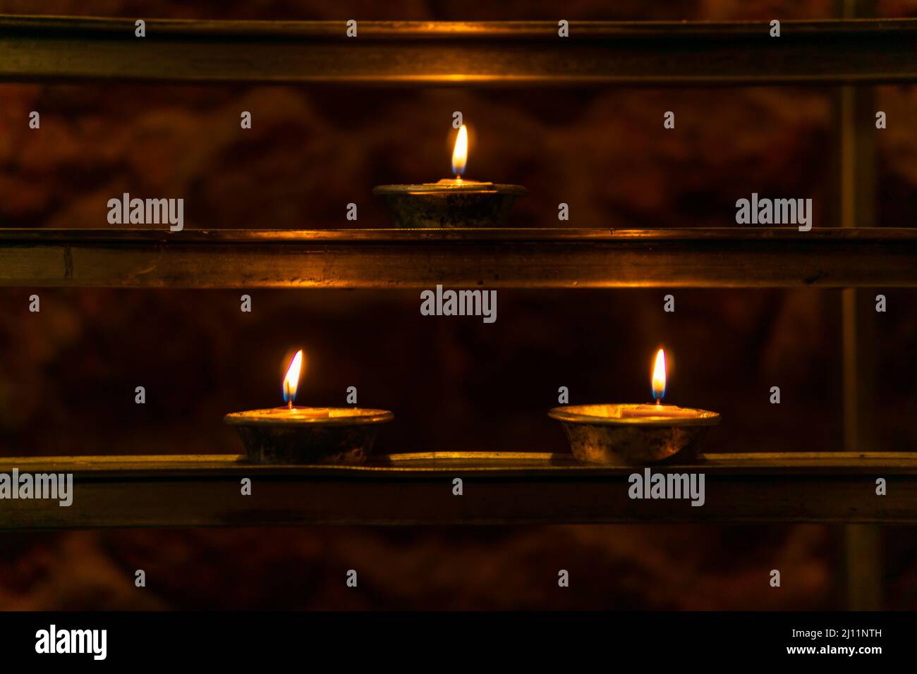 Tre candele votive illuminate su una rastrelliera votiva in una chiesa cattolica. Foto Stock