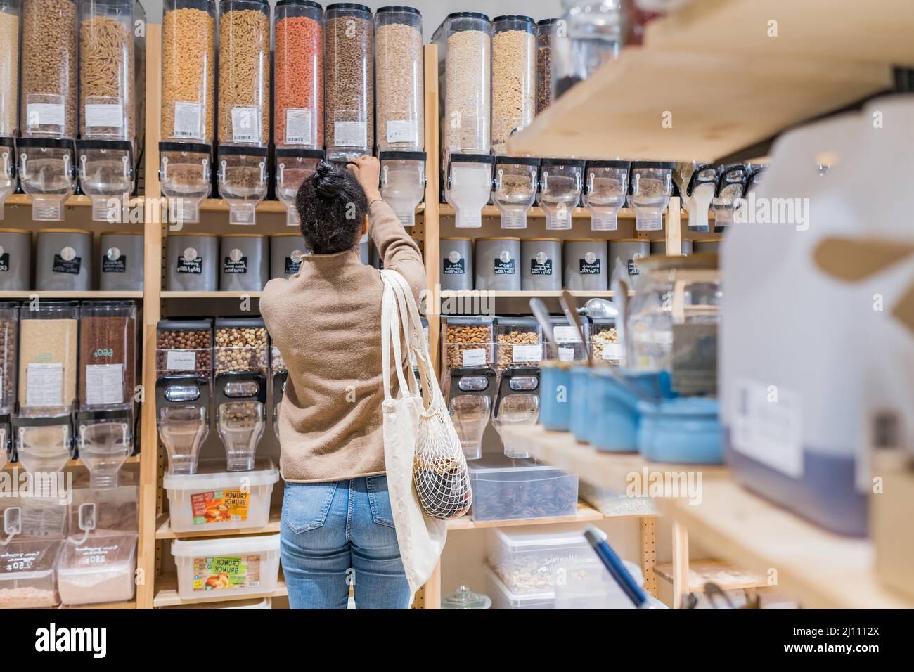 Donna afroamericana che acquista cereali biologici e cereali in un negozio di alimentari sostenibile zero rifiuti. Giovane donna che ricarica il contenitore riutilizzabile in locale Foto Stock