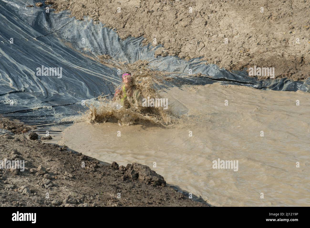 Una concorrente femminile nella corsa di Swampfoot 2014 scivola nella fanghetta con una grande barra. Foto Stock