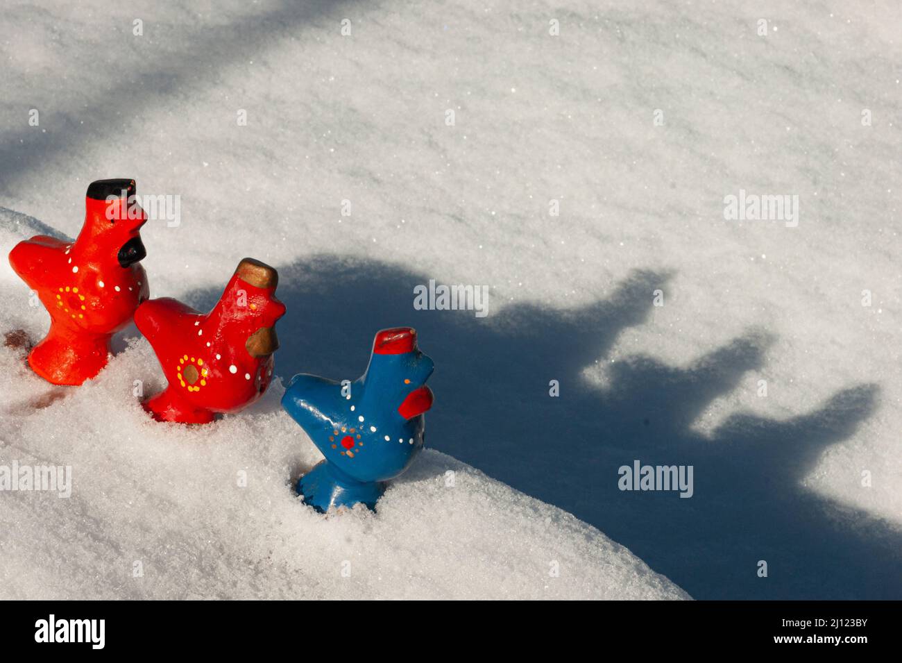 Vecchi uccelli di argilla o fischietti gettano le loro ombre nella neve. Sono un vecchio giocattolo per bambini dell'Europa dell'Est in arancione, rosso e blu. Spazio testo Foto Stock