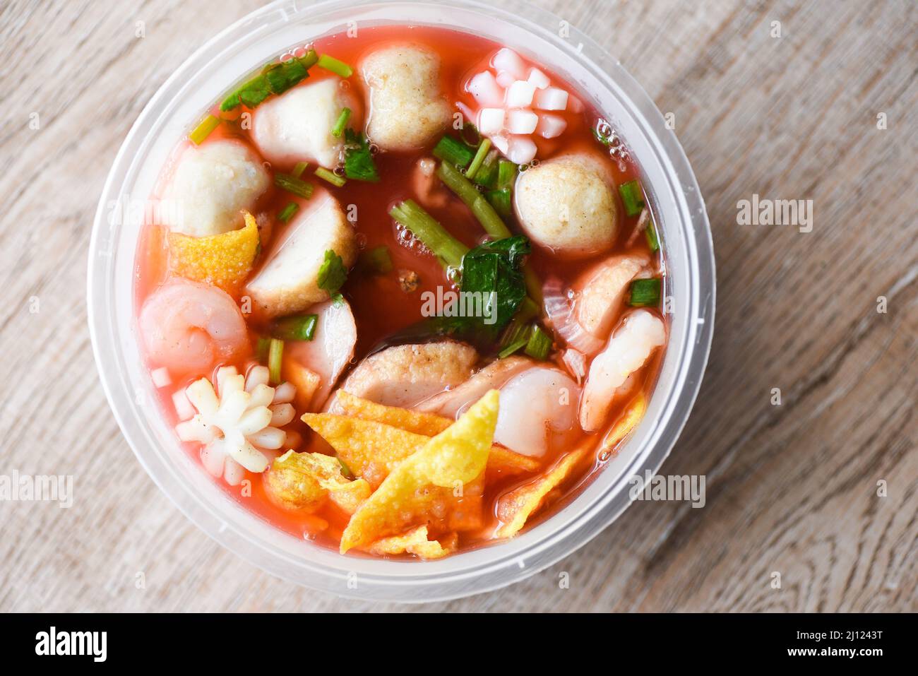 Zuppa rossa palle di maiale croccanti wontons con pesce calamari gamberi e palle di pesce verdure in zuppa ciotola plastica su tavolo di legno, vista dall'alto Thai e C. Foto Stock