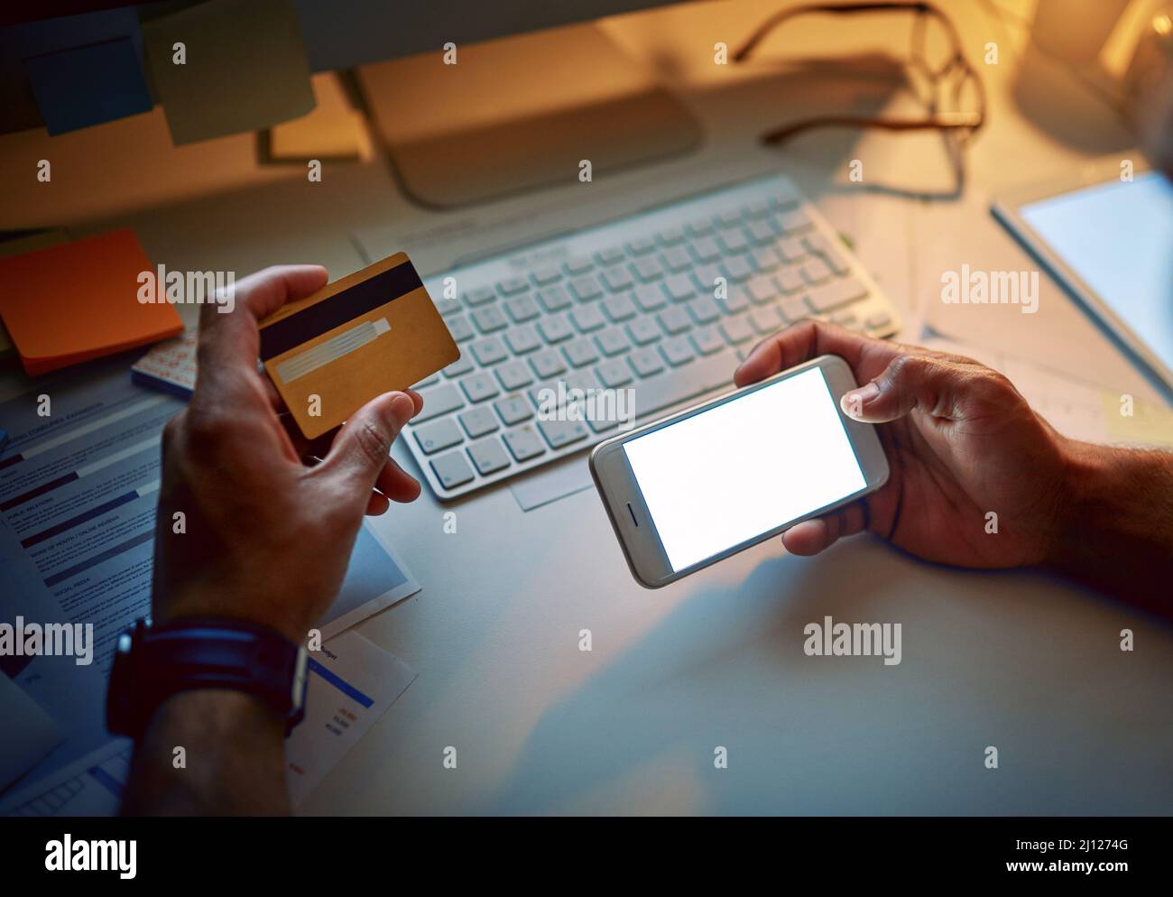 Ordinando il takeout per ottenerlo attraverso la notte. Scatto corto di un uomo d'affari irriconoscibile usando una carta di credito e un telefono cellulare durante una notte tarda Foto Stock