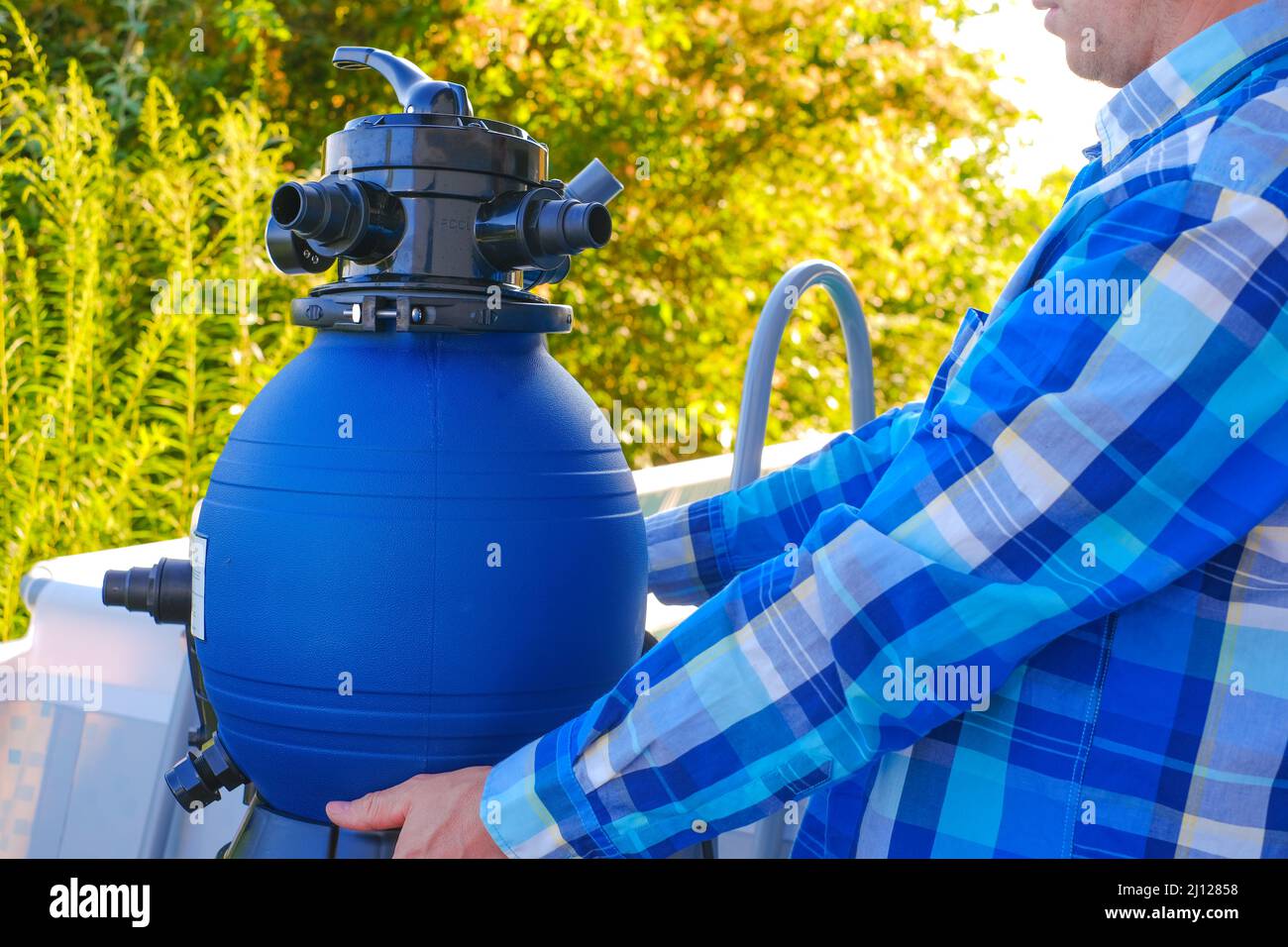 Piscina Filter.Swimming pool cleaning equipment. Filtro dell'acqua blu nelle mani di un uomo. Un uomo sposta i tubi flessibili verso il filtro nella piscina. Foto Stock