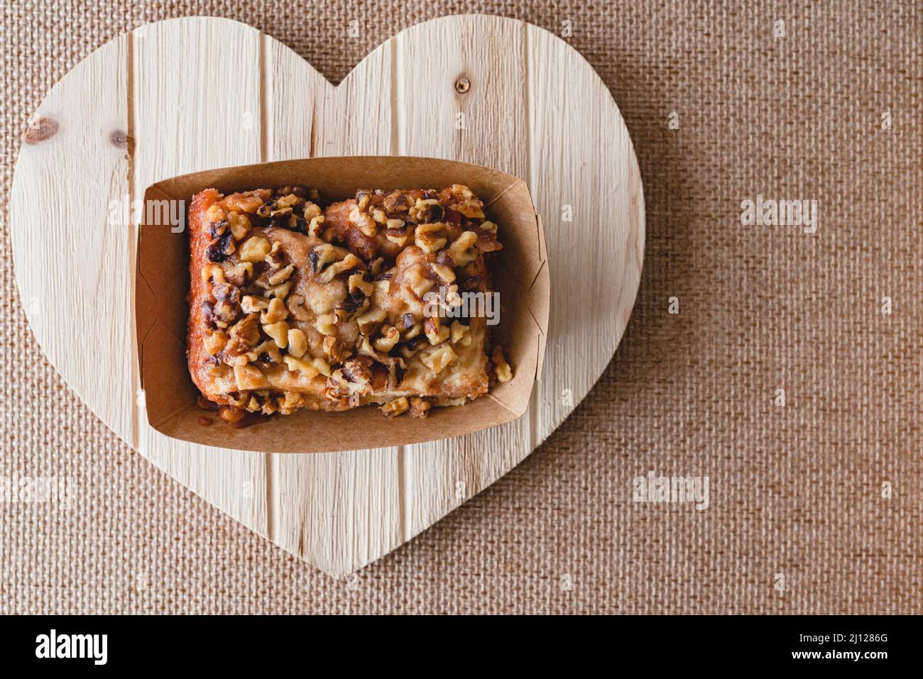 Rotolo di cannella di noce da vicino su un asse di legno a forma di cuore, posa piatta con spazio copia Foto Stock