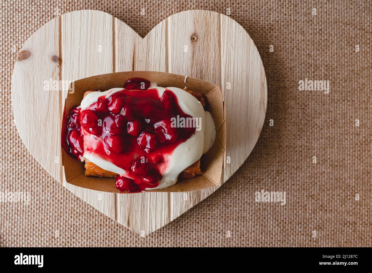 Rotolo di cannella Frosted Cherry da vicino su un pannello a forma di cuore in legno, piatto con spazio copia Foto Stock