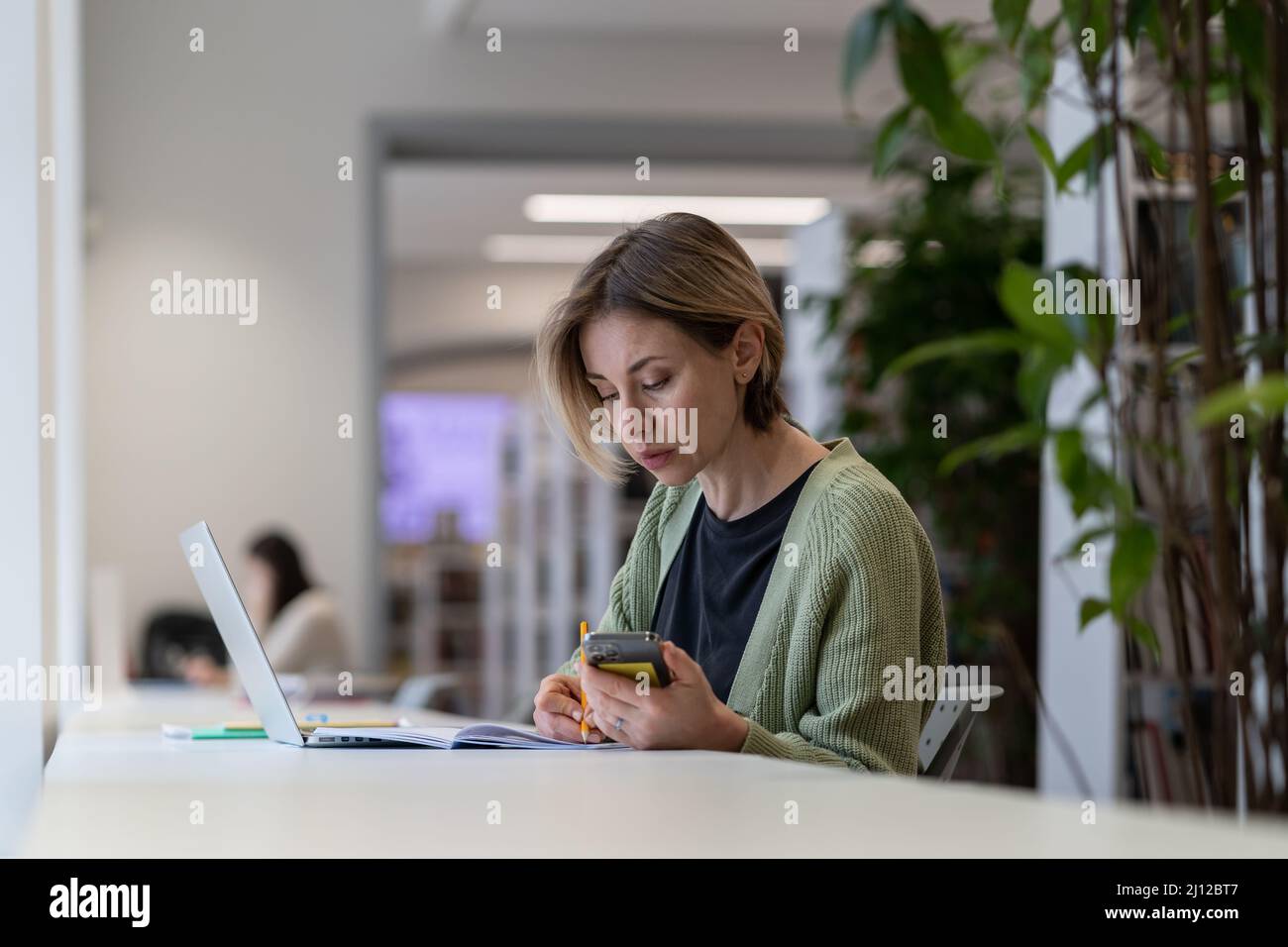 Insegnante universitario femminile concentrato utilizzando il laptop mentre si siede in una tranquilla e accogliente biblioteca Foto Stock