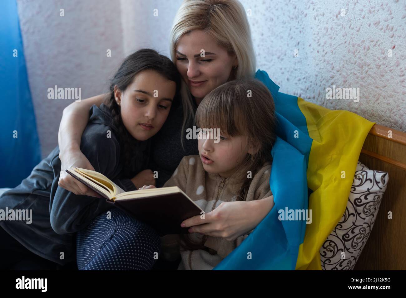 madre e figlia leggendo un libro con la bandiera dell'ucraina a letto Foto Stock