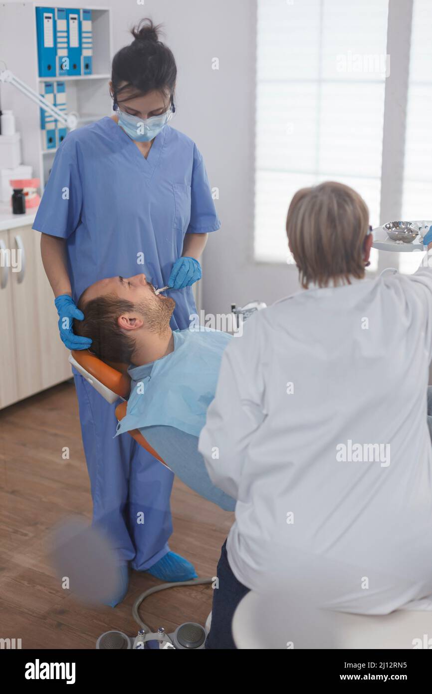 Assistente dentista che controlla la bocca del paziente analizzando l'infezione da carie utilizzando uno strumento stomatologico durante l'esame ortodontico in sala dentale. Concetto di procedura odontoiatrica Foto Stock