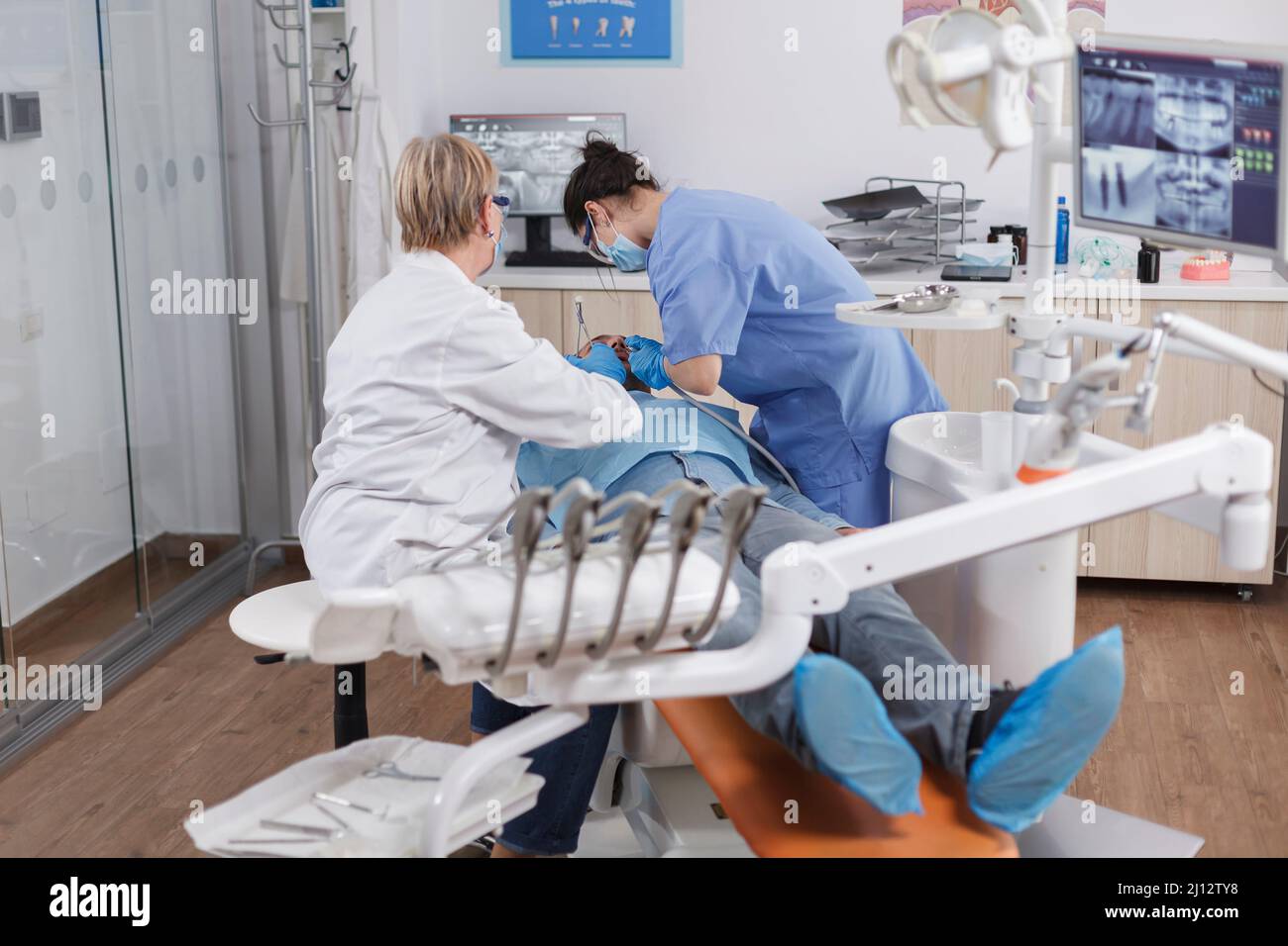 Il team di ortodontisti gestisce il paziente con le carie utilizzando strumenti dentali durante l'esame stomatologico in una sala d'ufficio odontoiatrica. Medico ortodontista che parla di trattamento delle infezioni con l'infermiere Foto Stock