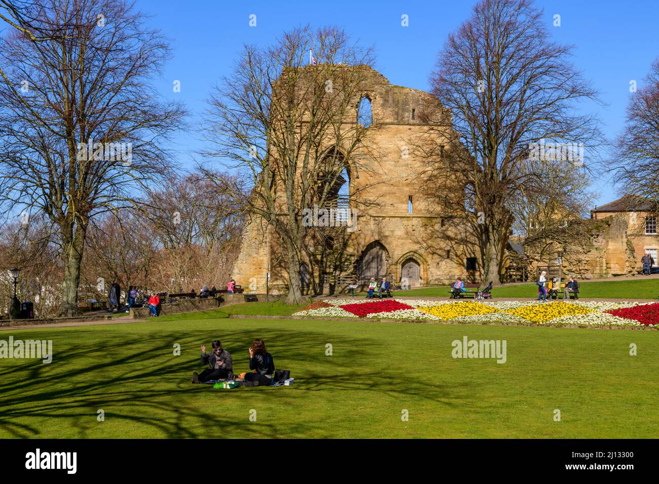 Le persone che si siedono rilassandosi godendo il sole (fiori di confine luminosi, antiche torri mantenere rovine, cielo blu) - Knaresborough Castle, North Yorkshire, Inghilterra, Regno Unito. Foto Stock