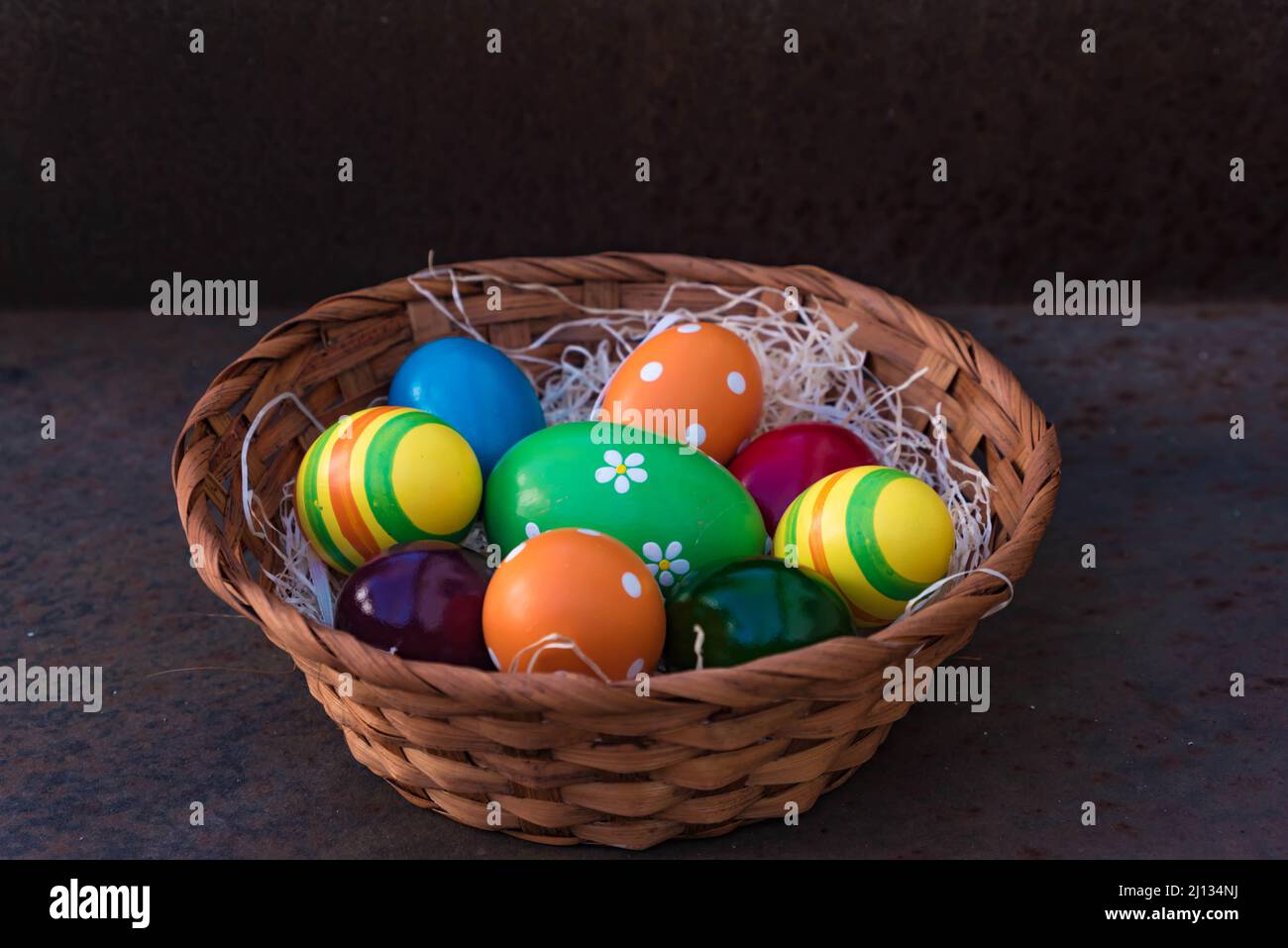 Cestino intrecciato di uova di pasqua colorate dipinte su un nido di lana di legno, isolato da sfondo scuro Foto Stock