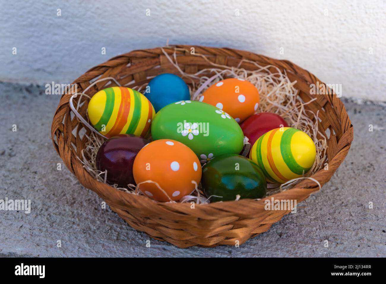 cestino intrecciato con uova di pasqua colorate in un nido di lana di legno, primo piano ed esposizione isolata Foto Stock